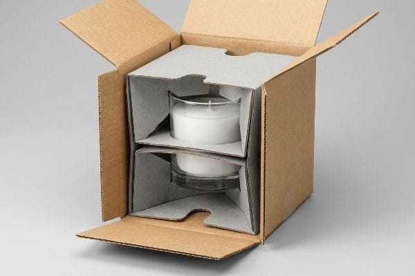 キャンドル包装用吊り下げ式挿入物 型抜きされた厚紙製のインサートが、可動式の茶色の段ボール箱に入った2つの白いガラス瓶キャンドルを保護している。.