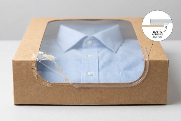 弾性接着緩衝材 青いシャツが見える透明な窓が付いたクラフト紙の箱。窓のパッチの張力を示す伸縮性接着剤バッファーの図が描かれている。.