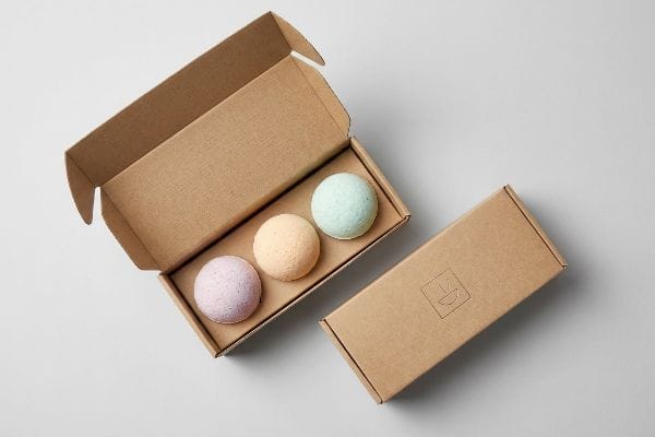 バスボムギフトセット パステルカラーのバスボムが、開いたクラフト紙の箱に入っており、閉じた箱にはさりげないロゴがあしらわれています。.