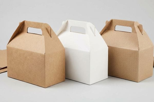ゲーブルボックスの材料 3つの切妻型箱(天然クラフト紙製1つ、白色の漂白硫酸塩紙製1つ、波型1つ)が、明るい地面の上に置かれている。.