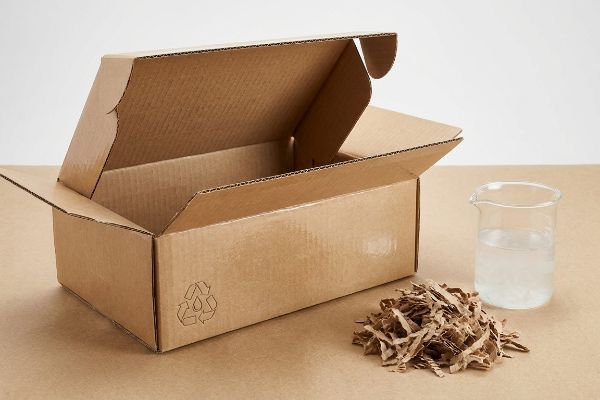 Corrugated Aqueous Repulping Materials Open corrugated board box with recycling symbol, shredded cardboard, and beaker of liquid, illustrating aqueous coating repulping.