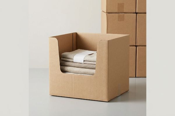 Brown corrugated open-top bin, an HSC, displays folded beige textiles with a white band, ready for retail.