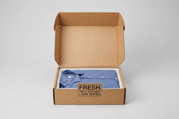Fresh 32ect Ista Tested Box Brown corrugated apparel mailer with a folded blue shirt on a white insert, stamped 'Fresh 32ECT Testliner - ISTA Tested'.