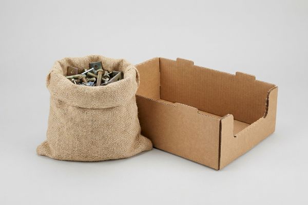 Burlap bag filled with assorted retail hardware, including bolts and brackets, next to an empty brown corrugated retail-ready tray.