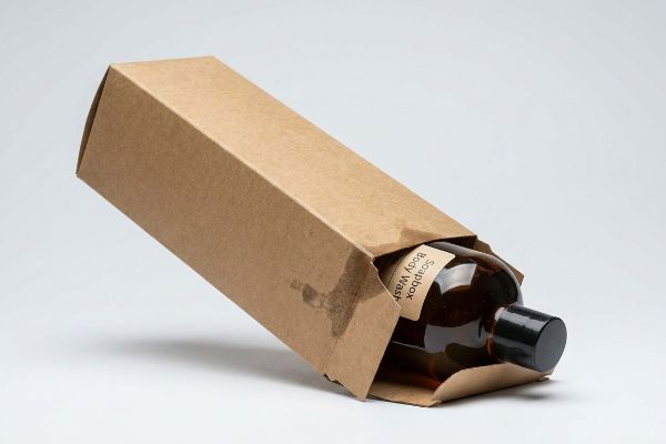 Brown kraft paperboard folding carton partially open, revealing an amber Soapbox Body Wash bottle with a black cap.